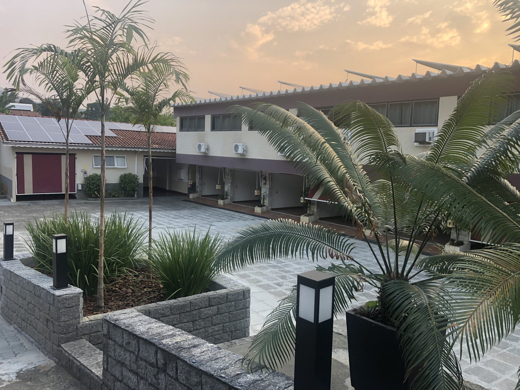 Pátio central do Motel Status ao entardecer, com palmeiras e jardins