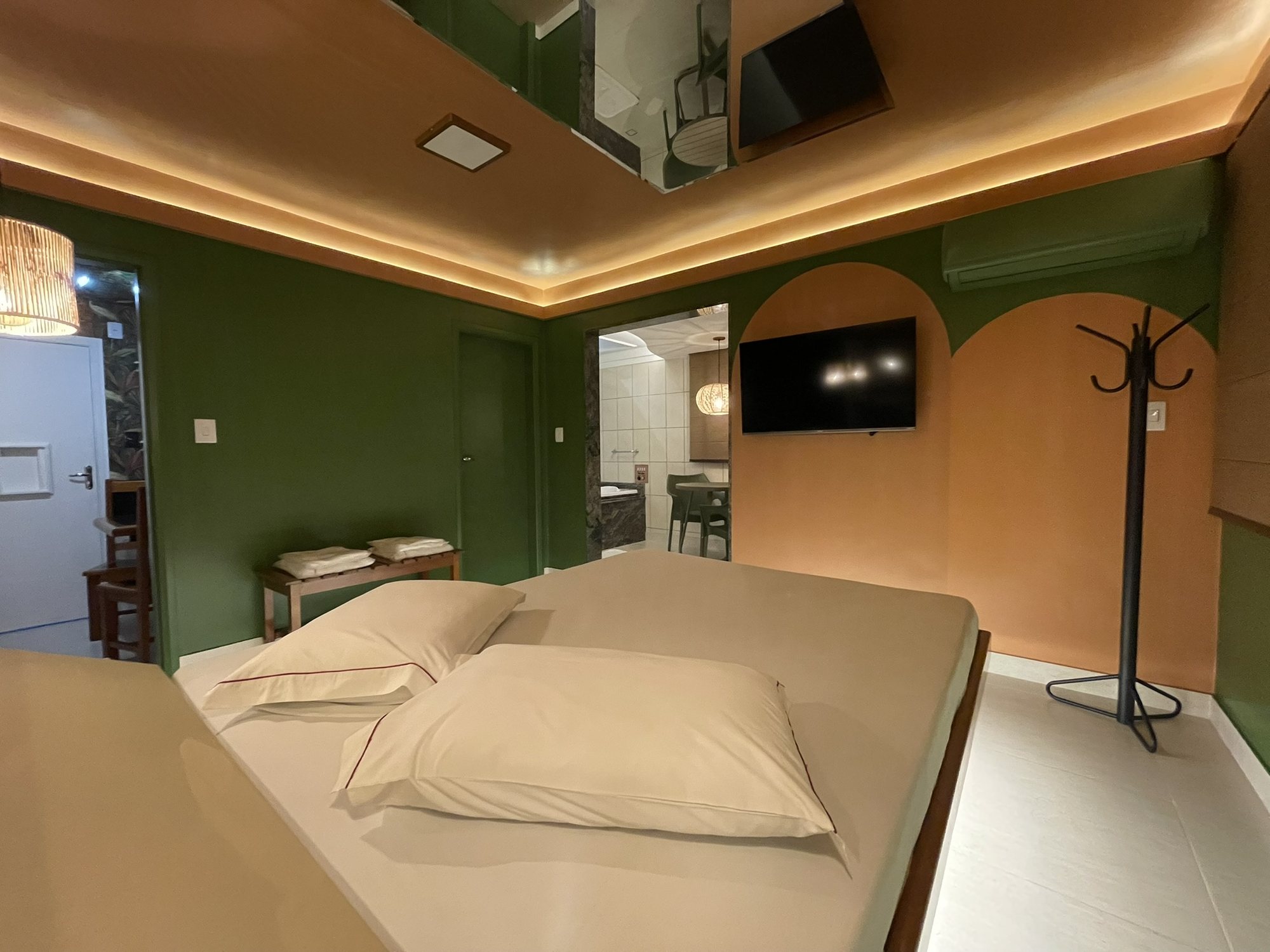 Suíte N: quarto com parede verde, arcos e Smart TV